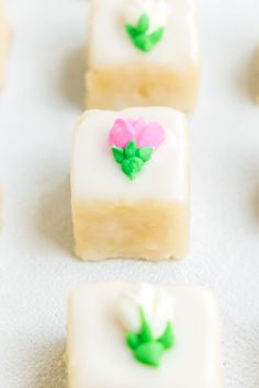 small square desserts with green leaves and pink flowers on them sitting on a white surface