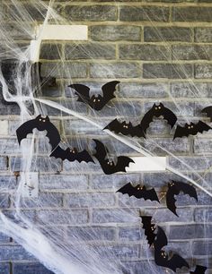 some bats hanging on a brick wall with spider webs around them and black bat decorations