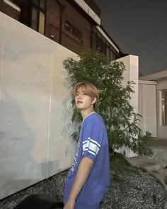 a boy standing in front of a white wall and some rocks with trees behind him