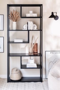 a black book shelf with books and vases on it in the corner of a room