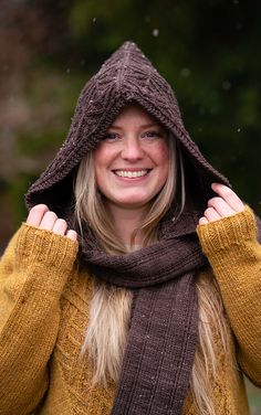 a woman wearing a brown hat and scarf with her hands on her head, smiling at the camera