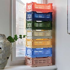 a stack of plastic crates sitting on top of a window sill next to a vase