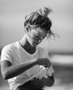 a black and white photo of a woman sitting on the beach with her hair blowing in the wind