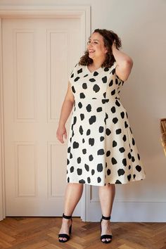 a woman standing in front of a door wearing a dress with black and white spots