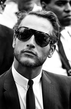 a man wearing sunglasses and a suit looks off to the side in front of other men