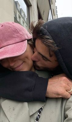 a man and woman kissing each other in front of a building with a pink hat on