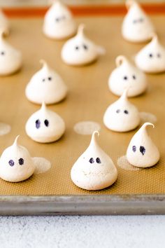 there are many little ghost shaped cookies on the baking sheet with eyes drawn on them