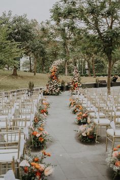 an outdoor ceremony setup with white chairs and orange flowers on the aisle, surrounded by trees