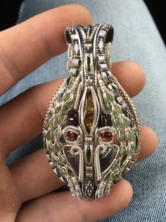 a person holding a silver ring with various colored stones in it's center and an intricate design on the front