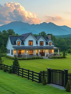 a large white house sitting in the middle of a lush green field with mountains behind it