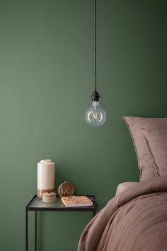 a bedroom with green walls and a lamp hanging from the ceiling over a small table