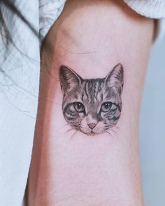 a cat's face is shown on the wrist and behind it is a small tattoo