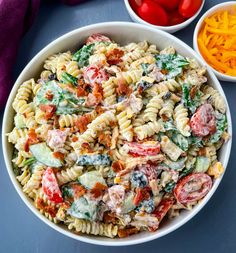 a bowl filled with pasta salad next to two bowls of cheese and tomatoes on the side