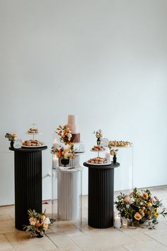 three black and white pedestals with flowers on them, one has a cake in the middle