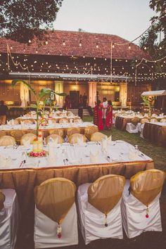 the tables are set up for an outdoor wedding reception with lights strung from above them