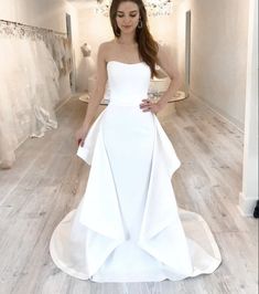 a woman in a white wedding dress standing on a wooden floor next to a chandelier