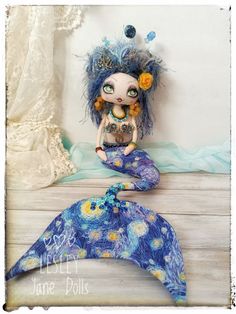 a doll sitting on top of a wooden floor next to a blue and yellow blanket