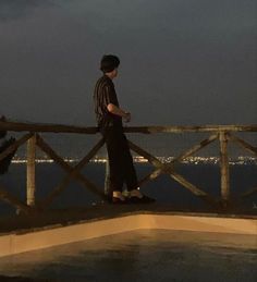 a man standing on top of a wooden bridge next to the ocean at night time