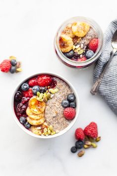 two bowls filled with fruit and cereal on top of a marble counter next to wooden spoons