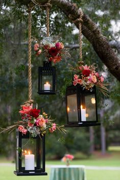 three hanging lanterns with flowers and candles are hung from a tree in front of a table