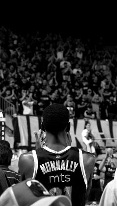 a man standing in front of a crowd with his hand up to his face while wearing a basketball uniform