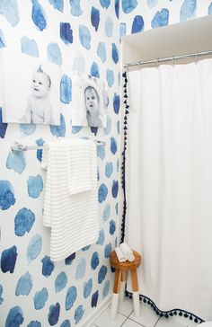 a bathroom with blue and white wallpaper, pictures on the wall and a stool