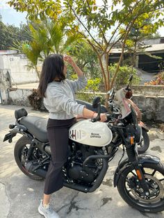 a woman standing next to a motorcycle on top of a cement ground with trees in the background