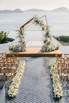 an outdoor ceremony set up with chairs and flowers on the aisle, overlooking the ocean