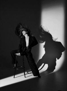 a woman is sitting on a chair with her hair flying in the air and she's casting a shadow