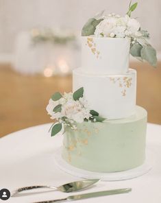 a wedding cake with white flowers and greenery sits on a table next to silverware