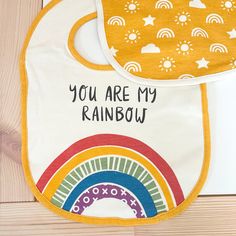 "A set of two cotton bibs featuring \"You Are My Rainbow\" sentiment with rainbow design and coordinating sky themed bib. Bib set includes adjustable metal snap closure and is machine-washable. The Rainbow bib set hangs on a single cardboard hanger. * 10″ x 14″ * Cotton, Metal * Cathy Heck Studio for Primitives By Kathy To see more products like these and our other products visit us online! We hope to see you soon.  www.mejmej.com" Playful Cotton Bib, Machine Washable, Playful Cotton Bib Machine Washable, Playful Cotton Bib As A Gift, Multicolor Washable Bib For Playtime, Cute Cotton Washable Bib, Cute Multicolor Machine Washable Bib, Multicolor Cotton Bib, Machine Washable, Cardboard Hanger, Fabric Wall Decals