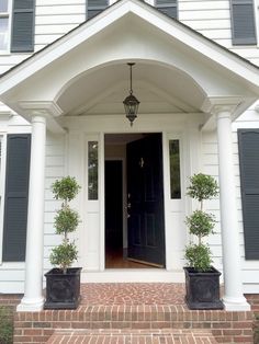 a white house with black shutters and potted plants on the front steps outside