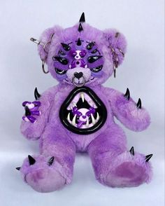 a purple teddy bear with black spikes on it's head and eyes, holding a tag in its mouth