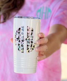 a woman holding a white coffee cup with leopard print on the side and pink shirt behind her