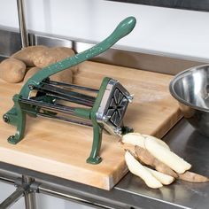 a potato slicer sitting on top of a wooden cutting board next to a metal bowl