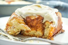 a piece of cinnamon roll with icing on a white plate next to a fork