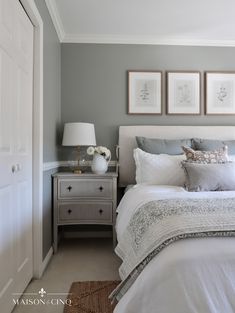 a bedroom with gray walls and white bedding, two framed pictures on the wall