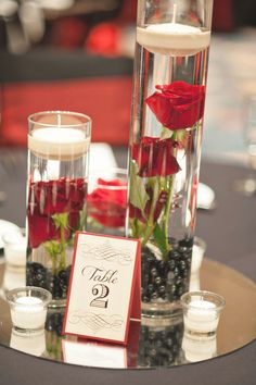 red roses and candles sit in glass vases on a round table with place cards