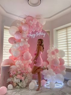 a woman standing in front of a birthday backdrop with pink and white balloons on it