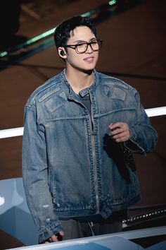 a young man wearing glasses and a denim jacket