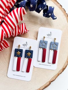 two red, white and blue earrings with stars are sitting on a piece of wood