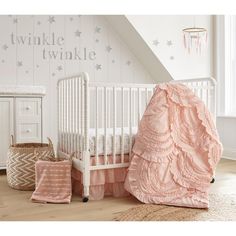 a white crib with pink bedding in a room under a slanted ceiling