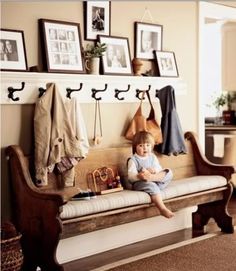 a young child sitting on a bench in front of a wall with pictures and coat hooks