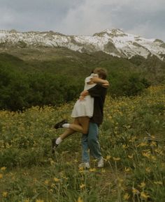 a man and woman hugging in a field with mountains in the background