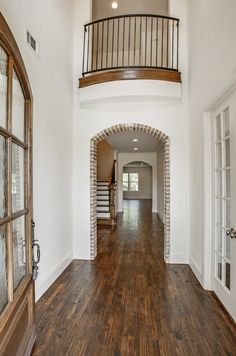 an empty house with wood floors and white walls, arched doorway leading to the second floor