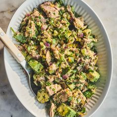 a white bowl filled with salad on top of a marble counter next to a wooden spoon