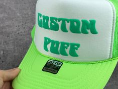 a person holding up a green and white hat with the words custom puff on it