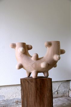 two wooden sculptures sitting on top of a piece of wood in front of a white wall