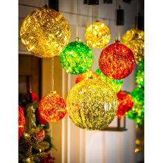 christmas balls hanging from the ceiling in front of a tree with lights on it and decorations around them