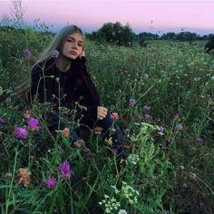 a woman sitting in the middle of a field with wildflowers on her knees